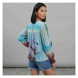 Woman wearing a colorful blouse with floral design and denim shorts against a gray background